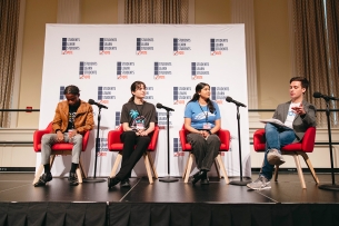 Four people sit in red chairs on stage