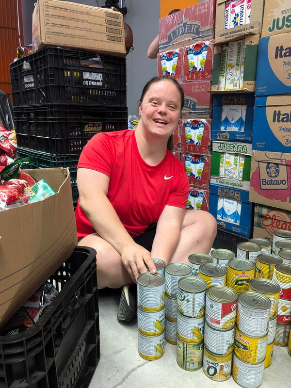 A young woman sits on the floor of a food pantry sorting cans.