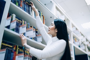 Asian woman picks a book off a shelf at a library