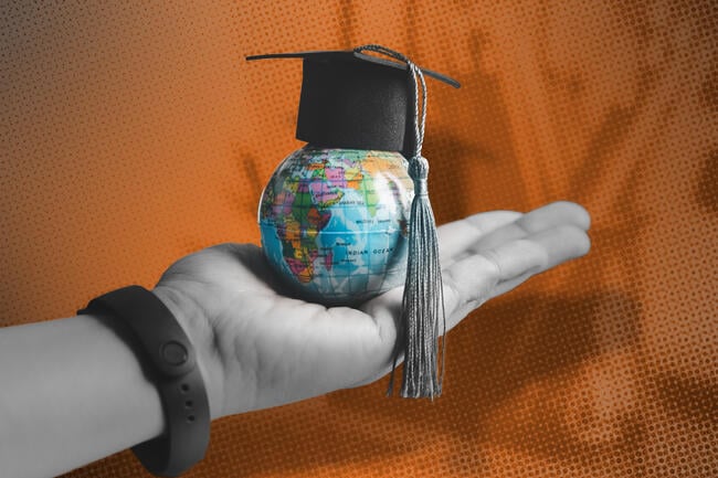A hand holding a small globe with a graduation cap on it. 