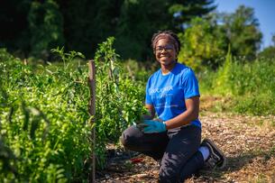 A student wearing a blue shirt poses in a garden. 