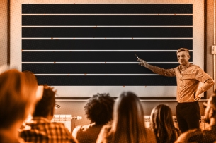 A photo illustration of a professor pointing to a whiteboard where all the text is redacted.