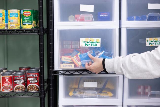 A student's hand reaches for a drawer of snacks labeled "two snacks per visit"