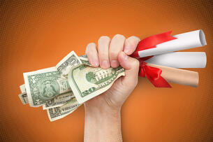 A fist is holding a wad of cash as well as several diplomas.