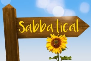 A wooden sign reading "sabbatical" in yellow letters, with a sunflower in front of it, against a sunny blue sky.