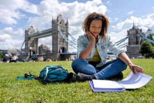 Happy student studying abroad in London sitting in front of Tower Bridge