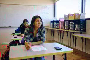 A student sits at a desk holding a pencil. 