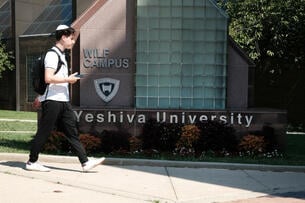 A student wearing a kippah walks in front of a sign that reads "Yeshiva University."