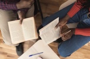 Hands of African American man and woman sitting at the library, reading and analyzing a novel together