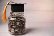 A jar full of coins with a graduation cap complete with tassel on top.