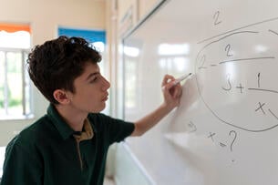 A young adult does a math problem on a whiteboard