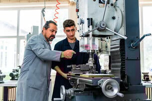 A teacher shows a student how to use a machine. 