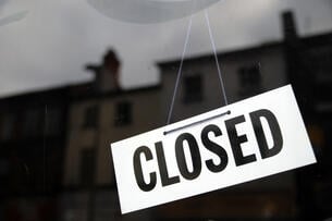 A photo of a hanging black and white "closed" sign, with a large building in the background.