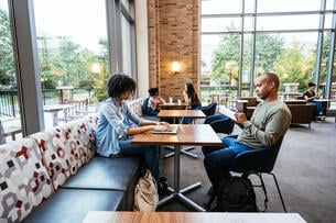 Two students work at a table in a large common area or library space