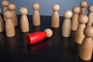 A single red pawn has toppled over and lies amid a group of wooden pawns.