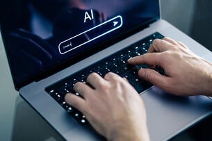 A close-up of hands typing on a laptop with the screen open to an AI chat bot.