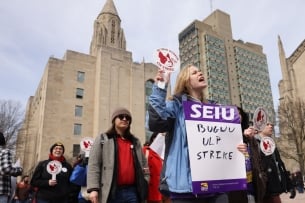 A photograph of demonstrators, with high rises in the background, holding signs supporting the Boston University Graduate Workers Union.