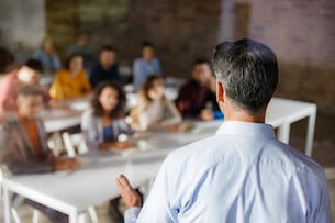 A rear-view photo of a male instructor giving a lecture to university students.