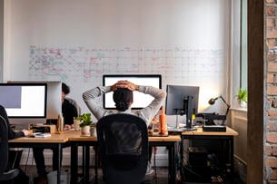 Young professional sits stressed working at a desk.