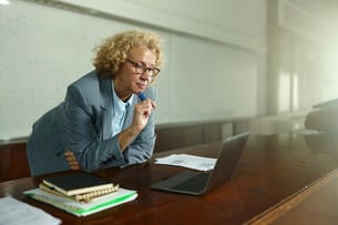 Female professor brainstorming while reading lecture plans on a computer in the classroom.
