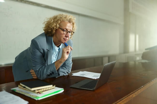 Female professor brainstorming while reading lecture plans on a computer in the classroom.