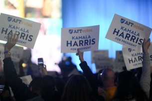The picture depicts a group of attendees gathered to hear Kamala Harris speak to the American Federation of Teachers convention in Houston last year. Three attendees hold up signs that say "AFT Votes: Kamala Harris for President."