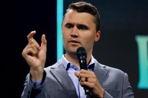 Charlie Kirk holds a microphone while speaking at a Turning Point USA event in 2024.
