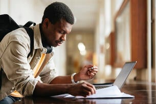 Focused university student engaging in study using a laptop in a bright hallway