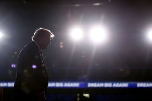A photograph of now president-elect Donald Trump walking across a darkened stage in Nevada in the closing days of the presidential campaign, on Oct. 31, with bright spotlight lights prominent in the background. Trump's face, however, remains in the dark. 