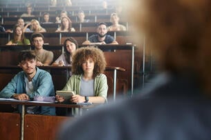 Crowd of university students listening to their professor during a lecture at amphitheater.