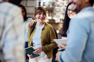 A photo of happy young students or postdocs socializing outside; the focus of the photo is a smiling young woman.