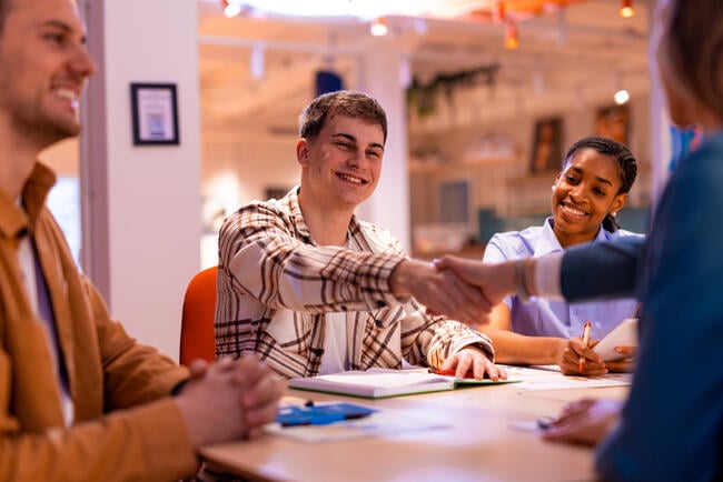 Young applicants shaking hands with a manager during a job interview in a modern office setting, exchanging smiles while discussing career opportunities and building professional connections