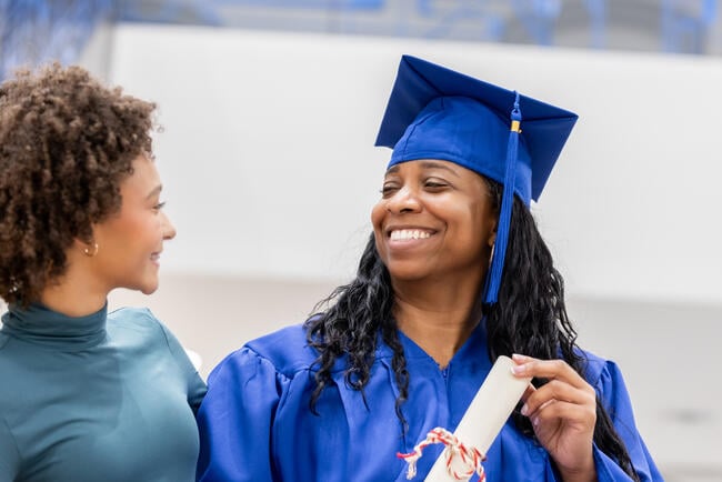 Woman holds diploma and smiles at daughter after graduation ceremony