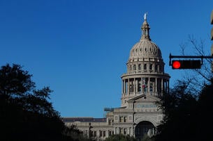 A photo of the Texas Capitol dome with a red stoplight in the foreground of the photo.