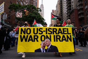 People marching down a street wave Palestinian flags and hold a banner saying "No US-Israel War on Iran," with photos of President Trump and Israeli prime minister Benjamin Netanyahu on it.