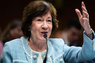 A photograph of Sen. Susan Collins speaking into a mic and gesturing with her left arm.