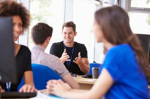 A counselor is speaking to a male student. Two women are in the foreground but are not the subject of the photo.
