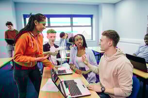 A young woman shows her classmates a 3-D wind turbine model in their engineering class. Both of the students are using a laptop.