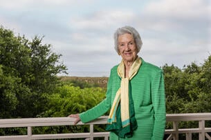 Jane Batten smiles at the camera while wearing a green jacket and yellow scarf.