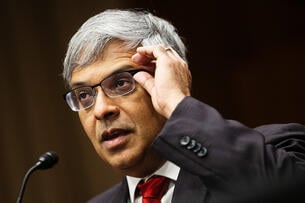 Jayanta Bhattacharya, a man with silver hair and glasses wearing a suit and red tie