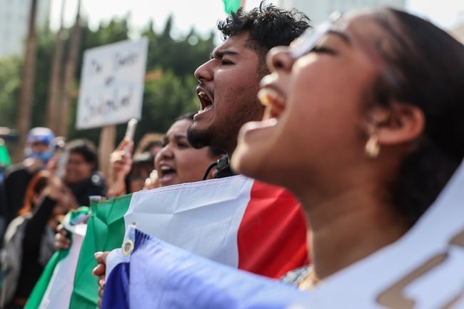 A young woman and man shouting, holding signs and flags, while protesting Trump's immigration policies in Los Angeles. 