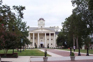 A building with columns on a green with a brick path at Limestone University