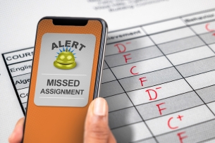 A phone reads "alert! missed assignment" in front of a report card featuring low grades—F's through C-pluses.