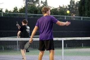 Two male students play pickleball on a court. 