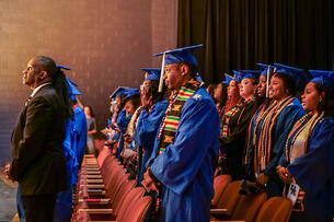 Students in blue caps and gowns gather at the Senior Salute event hosted at the Lyric Theatre.