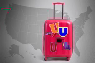 A suitcase with university stickers in front of a map of the United States.
