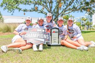 Five women pose outside with a golf championship trophy
