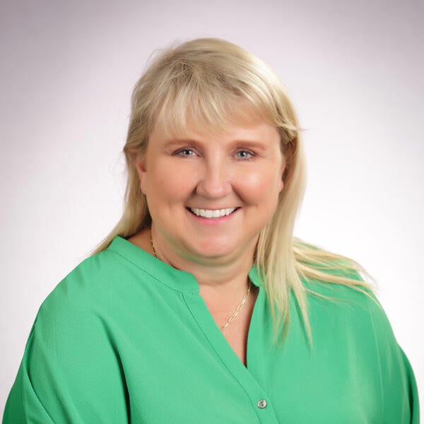 Tracy Teater smiles for a headshot wearing a green blouse against a white background