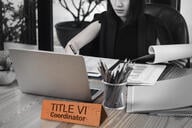 A woman works behind a desk with a nameplate that says "Title VI coordinator."