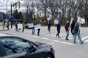 A photograph of demonstrators, holding signs, walking across a crosswalk.